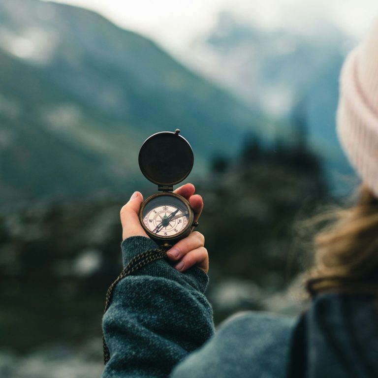 Orientierung Eine Frau blickt auf einen Kompass in ihrer Hand, im Hintergrund wunderschöne Berge.